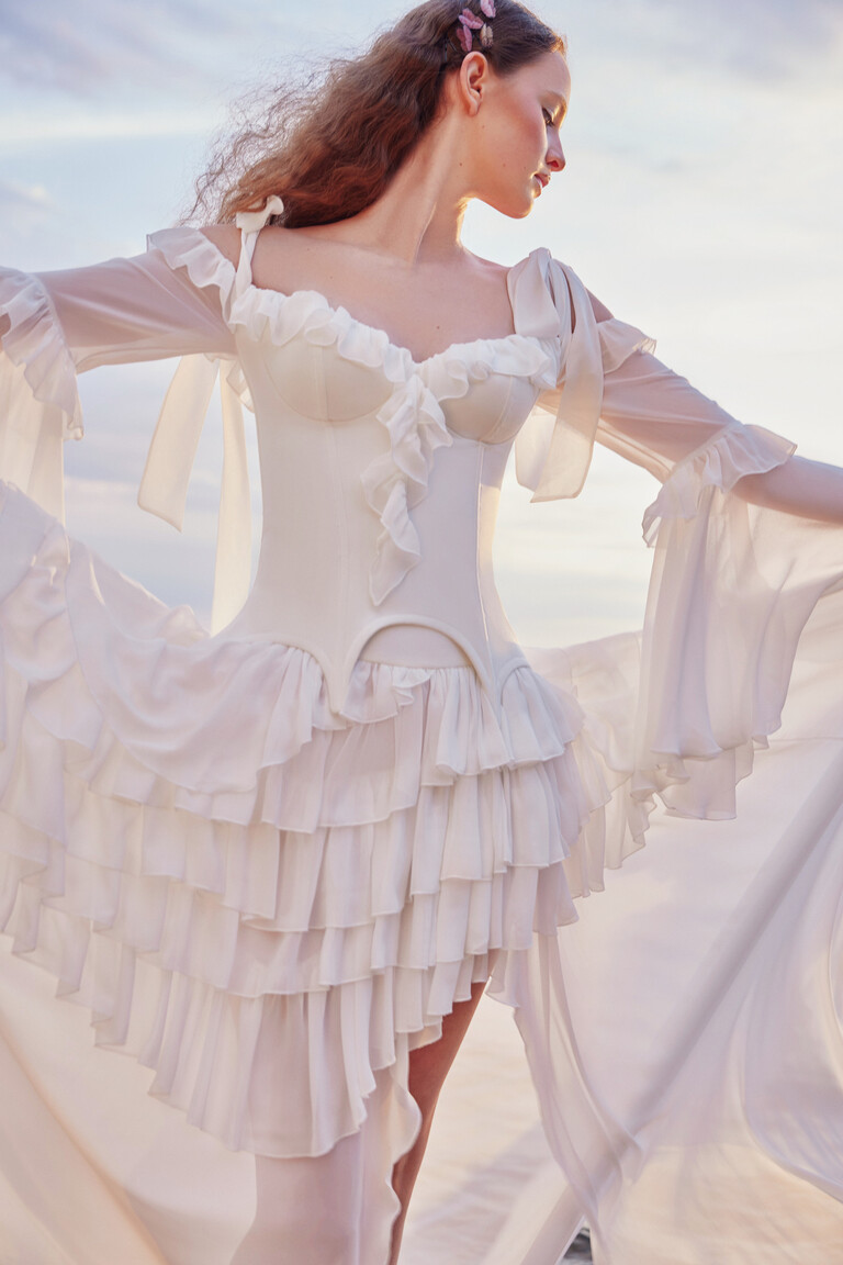 Riot beach wedding dress front view with asymmetrical high-low ruffled skirt against sky