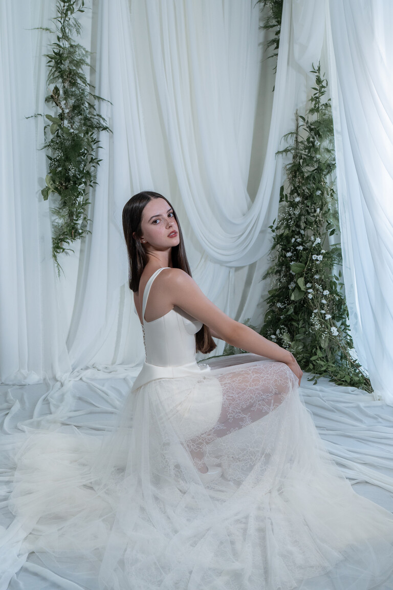 Crouching bride wearing Emily dress showing lace-up back and spread out sheer lace train
