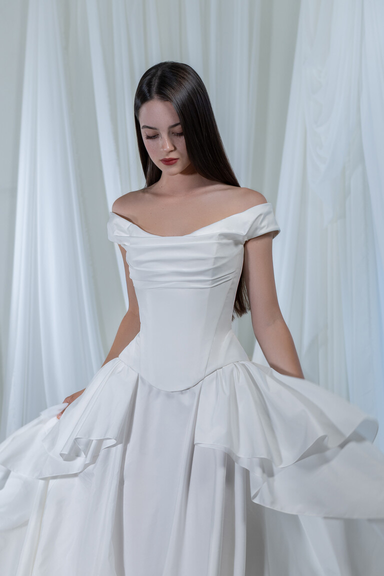 Paradise dress front view highlighting sculptural corset bodice and draped off-shoulder sleeves