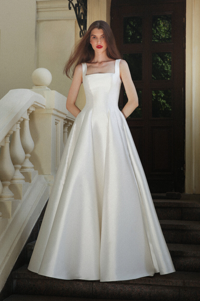 Jolie off-white Mikado wedding dress front view featuring square neckline and wide straps on stone steps