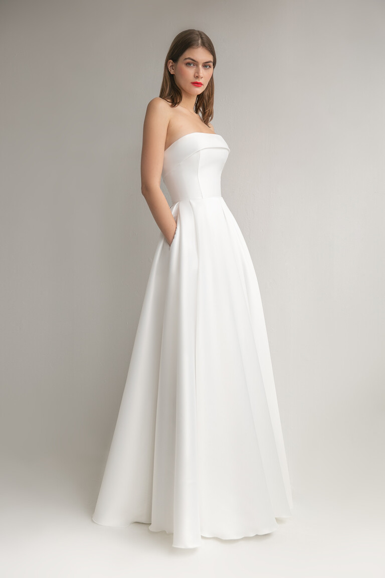 Three quarter view of Sophie ivory Mikado gown highlighting side pockets and strapless flap bodice