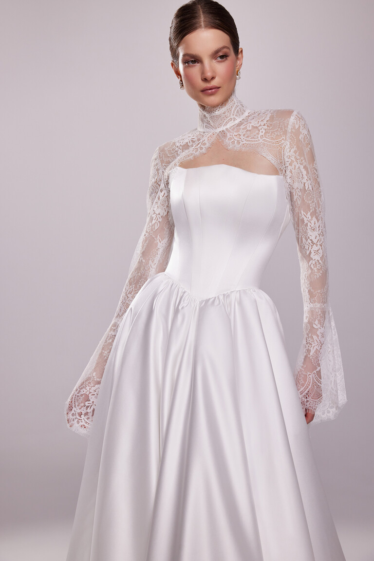 Model wearing the ivory Tessa Bolero with long sleeves, showcasing the sheer lace overlay and flared cuffs from the front.