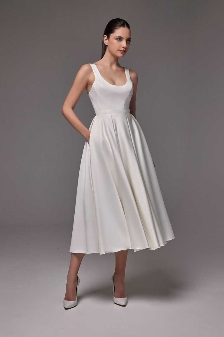 The Unona Barbara midi ivory dress in full, highlighting the graceful flare of its tea-length A-line skirt with pockets.