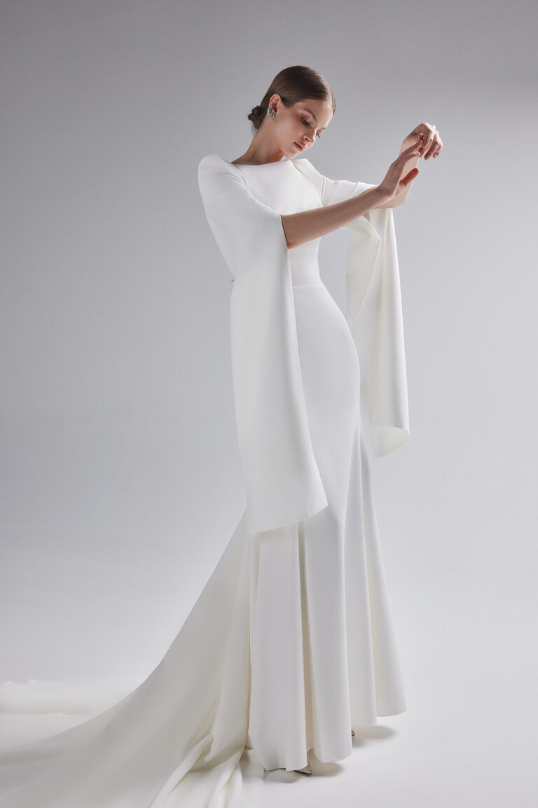 Side angle of Ashley crepe wedding dress featuring floor length split cape sleeves