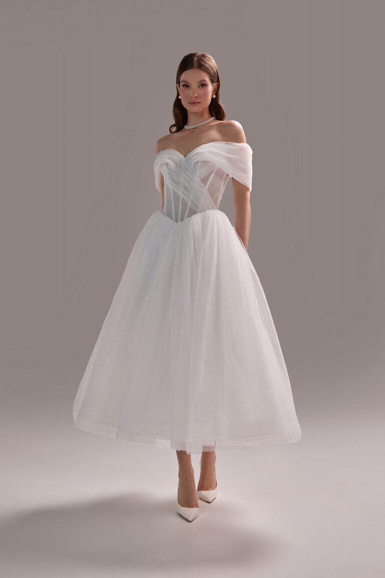 Full view of the Tutu Midi tea-length dress by Unona. Ivory A-line gown with an off-shoulder corset top and pleated tulle.