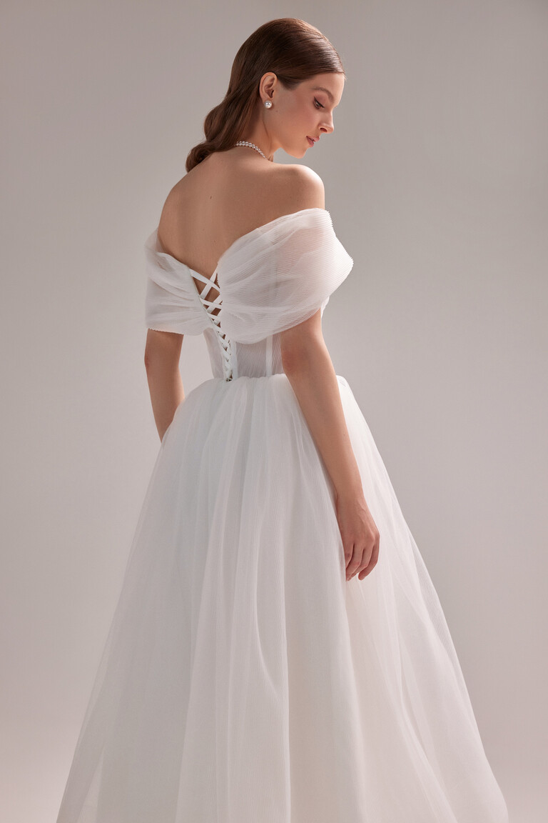 Back three-quarter view of the Tutu Midi dress in ivory. Showcasing the corset lace-up closure and voluminous pleated tulle.