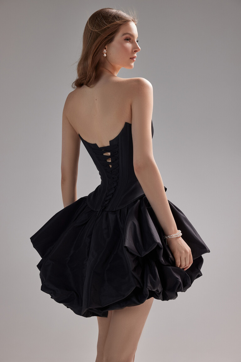 Model showing the three-quarter back view of the Amira Mini black taffeta dress with its detailed lace-up corset closure