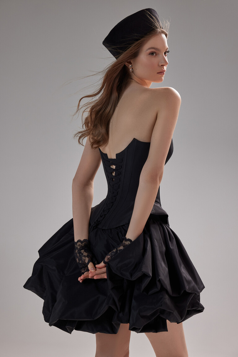 Back view of the styled Unona Amira Mini black dress showing the lace-up corset and bubble skirt with formal accessories