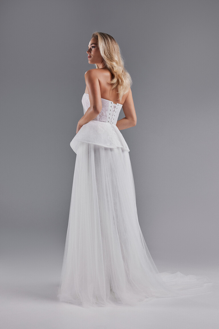 Alla dress rear three-quarter view showing lace-up back, peplum, and tulle skirt