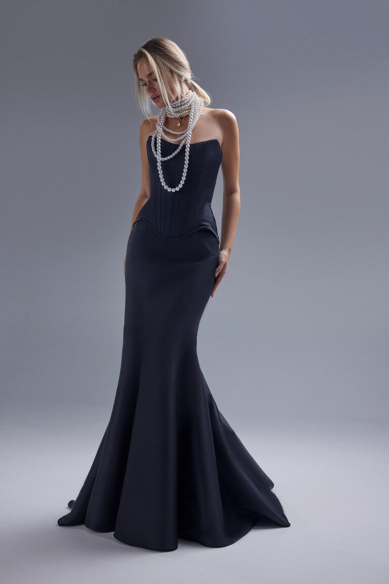 A three-quarter view of the Pina black evening gown highlighting the structured corset bodice and the dramatic mermaid silhouette.