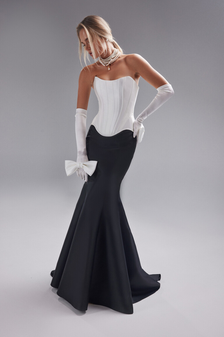 Unona Pina gown full view featuring an ivory corset top black mermaid skirt and a large white bow accessory on the hip.
