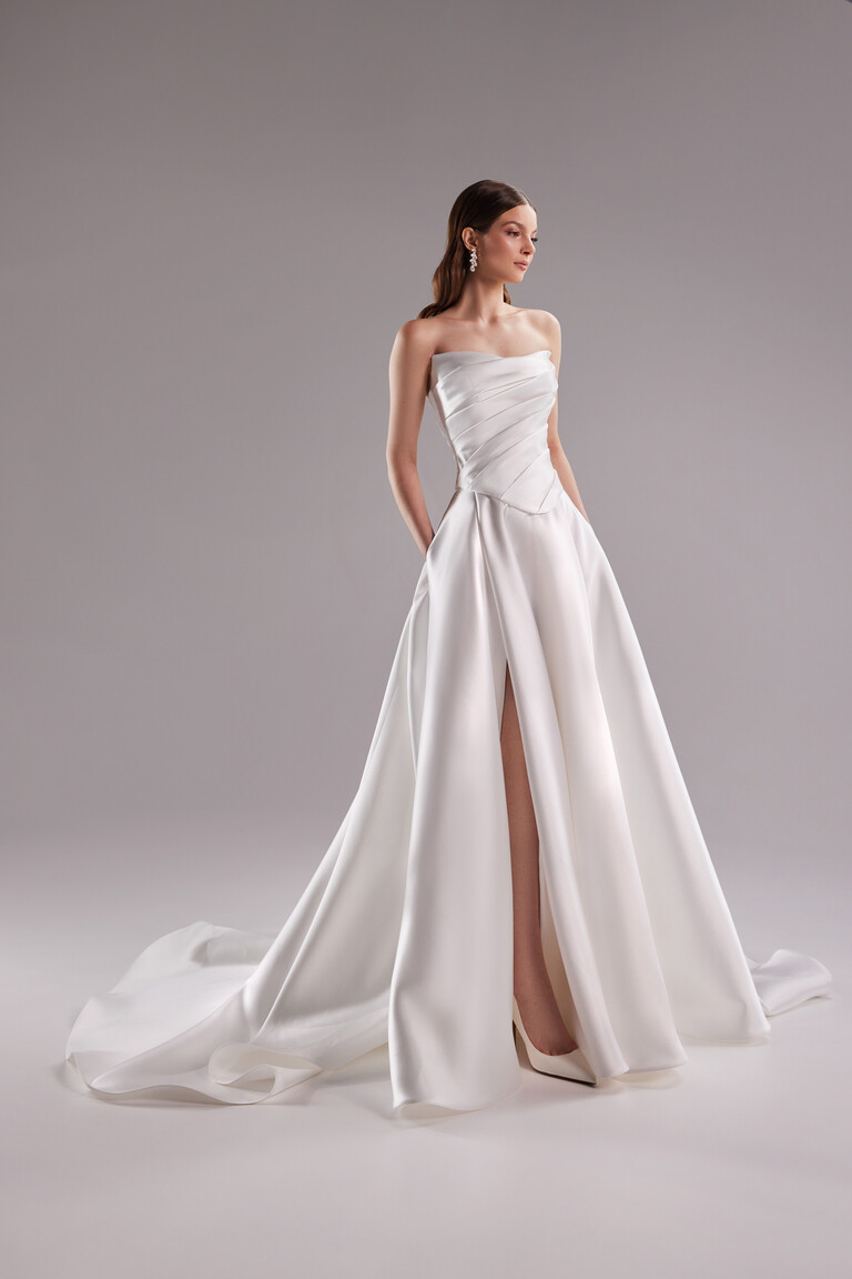 Angled view of Tori satin bridal gown featuring high slit and hidden side pockets