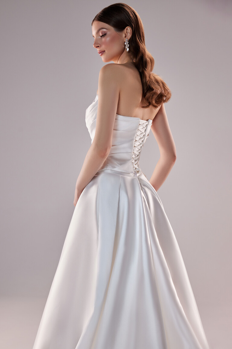 Three quarter back view of Tori dress featuring corset lacing and pleated ivory satin skirt