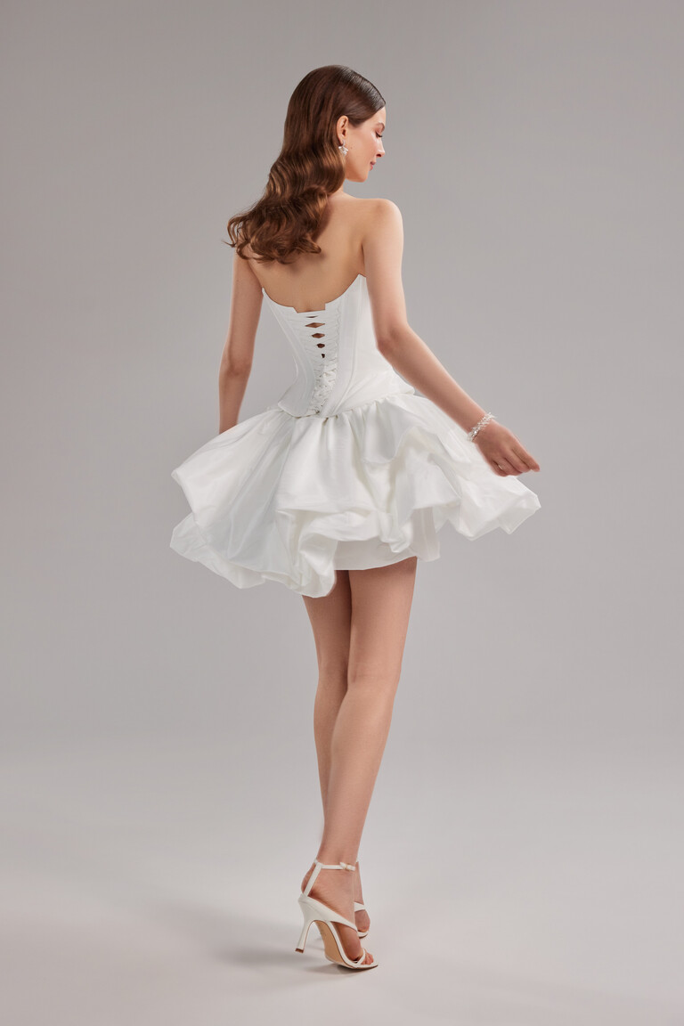 The Amira Mini short ivory wedding dress by Unona seen from the back, showing the full lace-up corset and puffy taffeta skirt.
