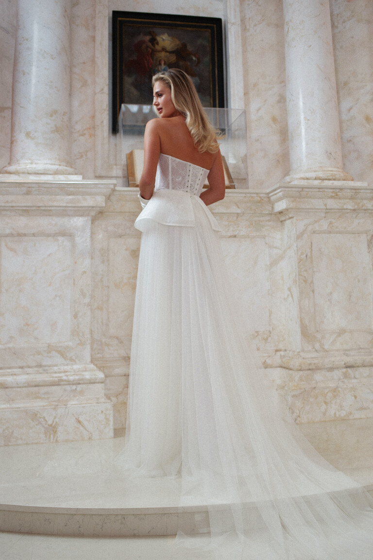 Back view of Alla bridal gown with long tulle train and corset lacing in marble room