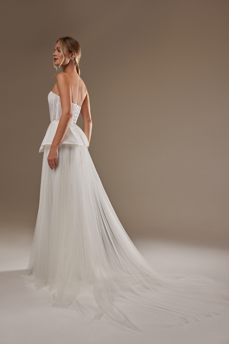 Rear angle of Alla wedding dress showing lace-up corset, peplum, and flowing tulle train