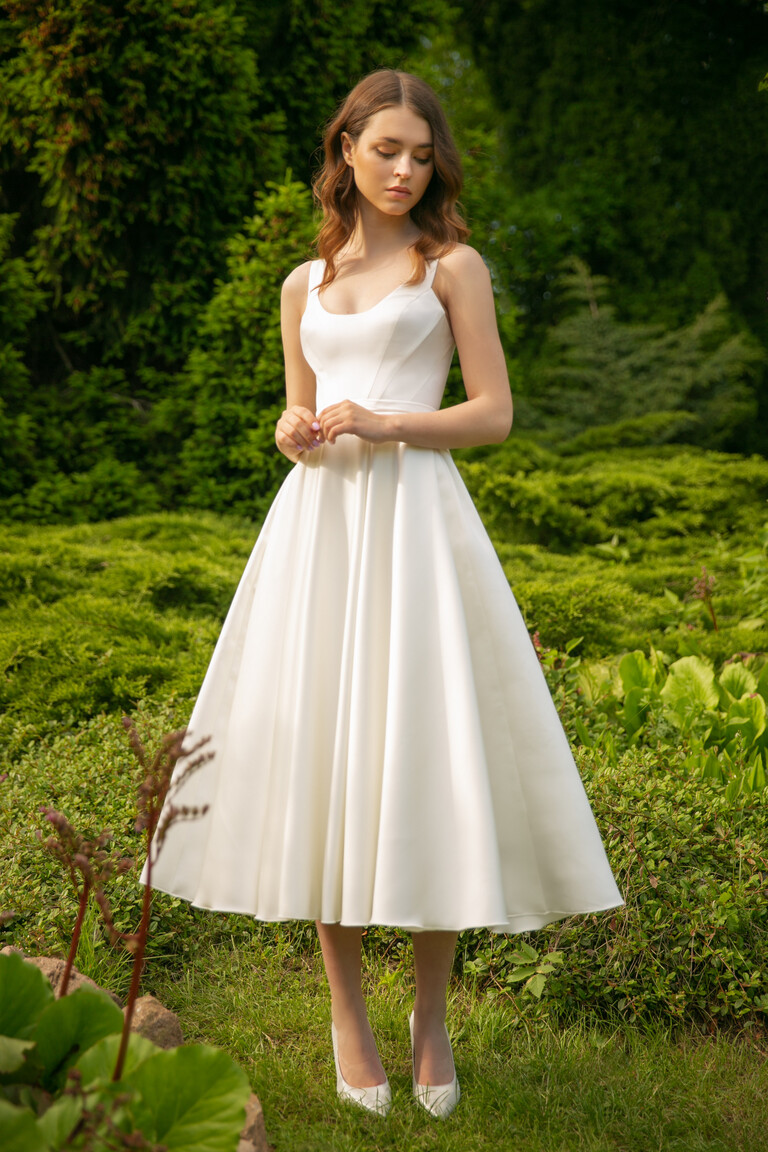 Unona Barbara midi ivory wedding dress worn outdoors, full front view against a lush green background showing its classic style.