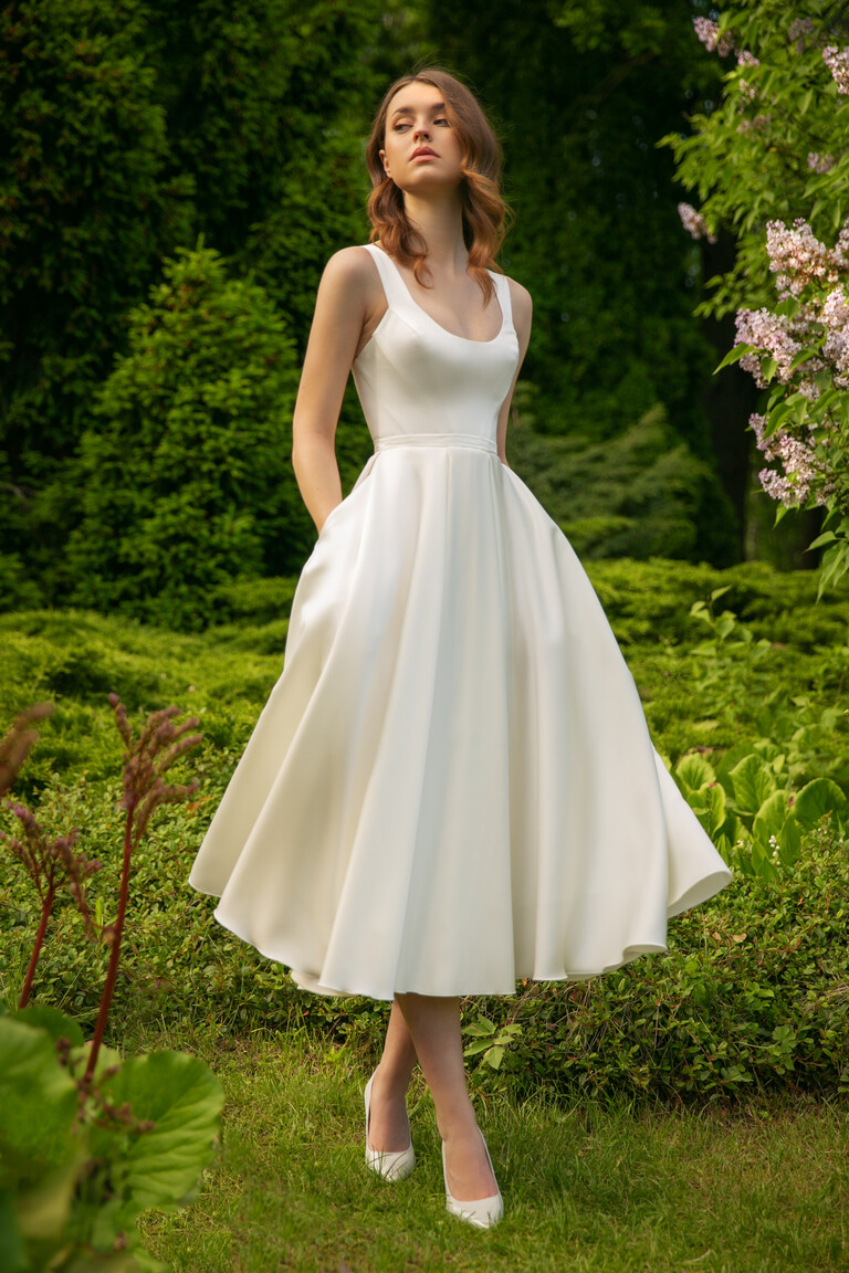 Model wears the Unona Barbara midi ivory dress in an outdoor garden, showcasing its A-line skirt and practical side pockets.