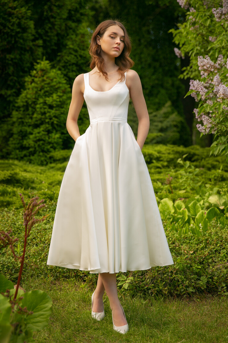 Front view of the Barbara midi A-line dress with pockets, worn in a beautiful garden setting for an engagement or party.