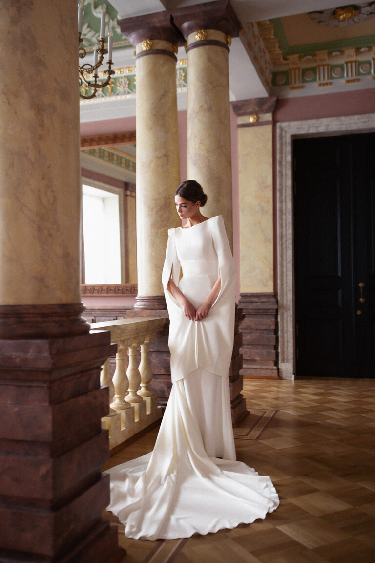 Unona Ashley modern wedding dress with cape sleeves standing in grand hall