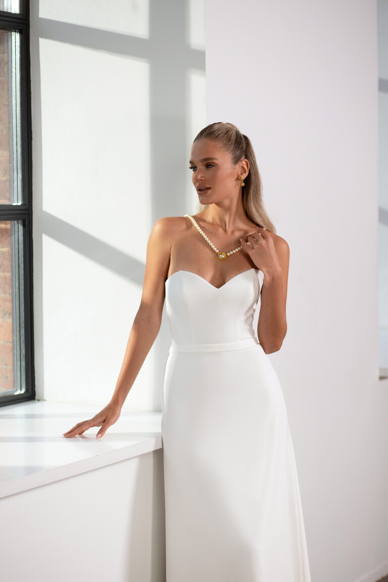 Three-quarter view of Adeline fitted crepe wedding dress near large window