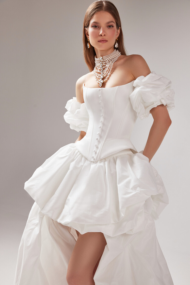 Model wearing the Unona Amber off-white wedding dress with puff sleeves, showing the sculpted corset and side pockets in the skirt.