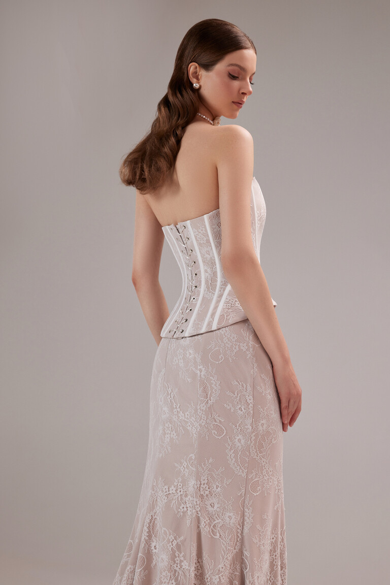 Three-quarter back angle of the Unona Prima gown, detailing the lace-up corset closure and the elegant floor-length lace skirt.