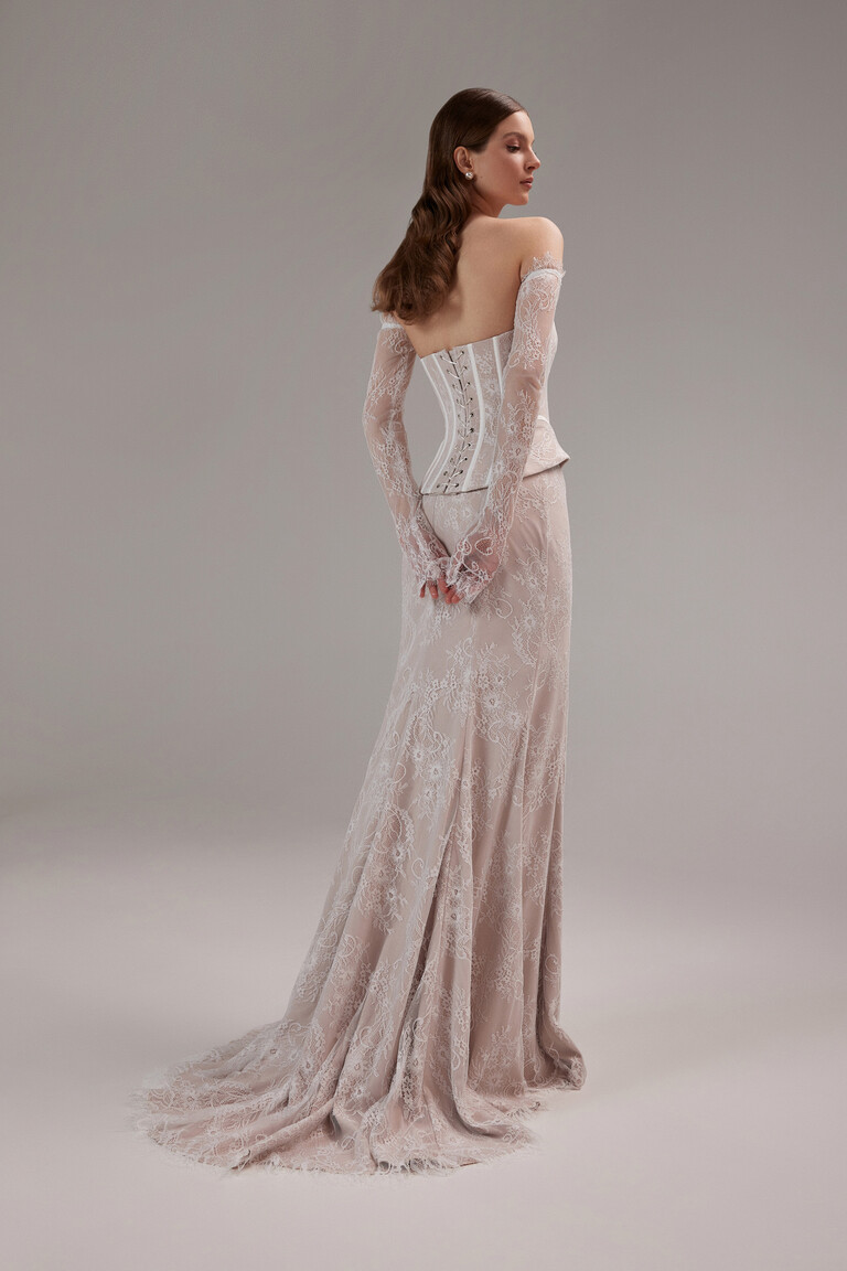Full-length three-quarter back view of the Unona Prima lace gown with a lace-up corset and skirt with a small train.