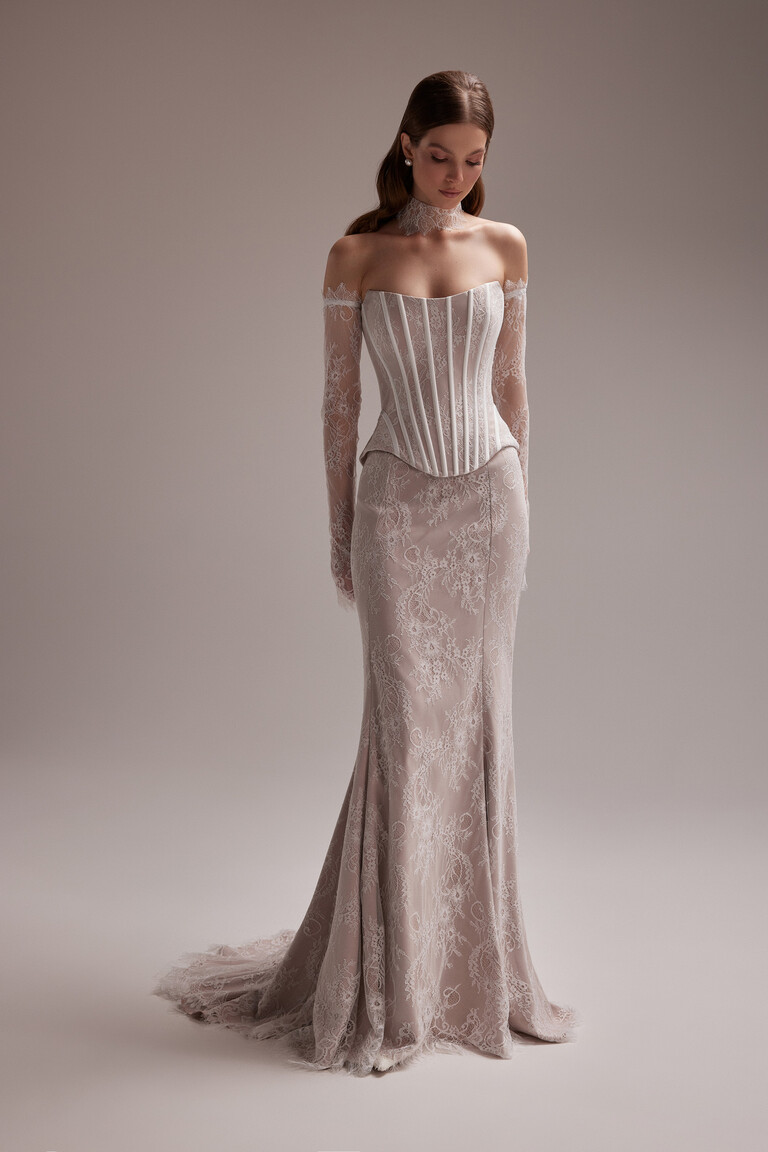 Model wearing Unona Prima beige lace bridal gown with a strapless corset top detachable sleeves and matching choker.