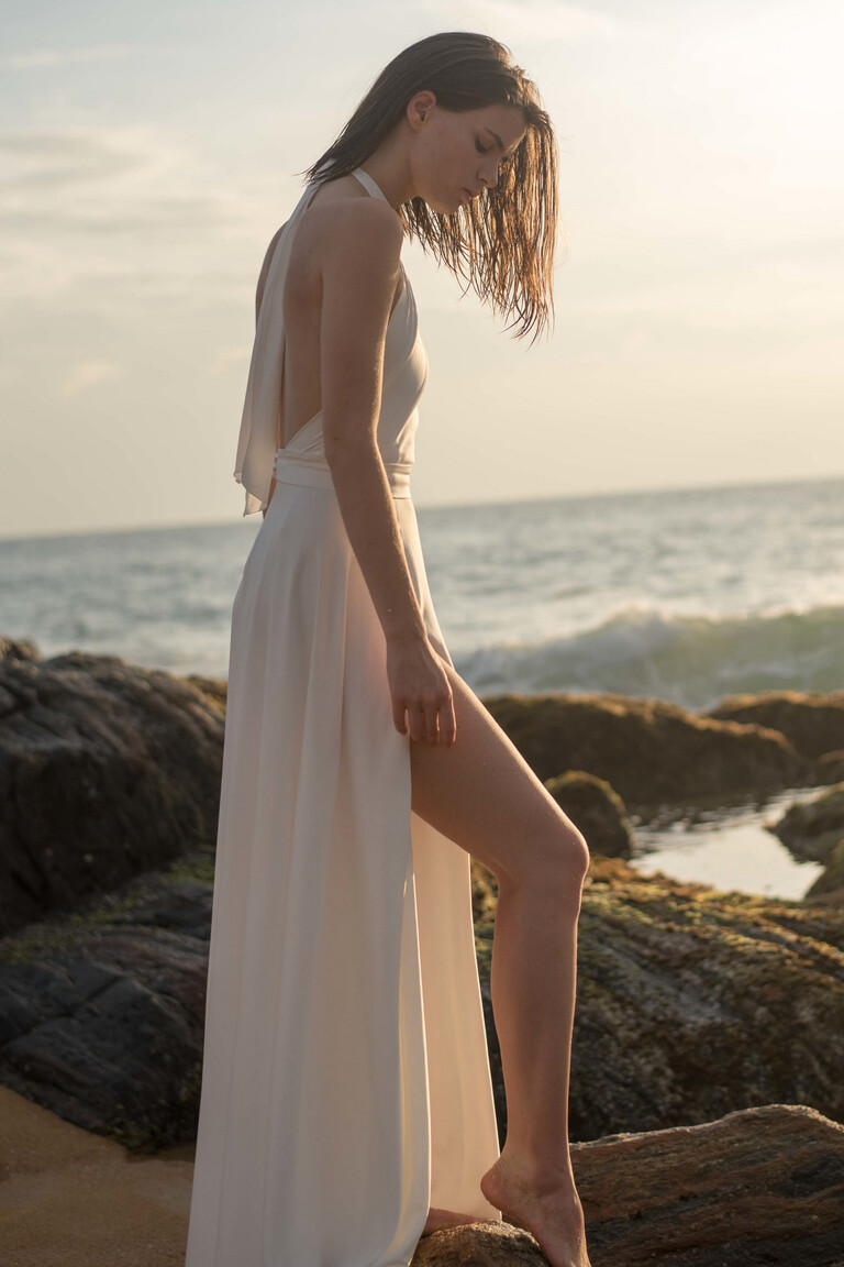 Side view of the Unona Mary ivory silk wedding dress showing its open back and high slit at sunset