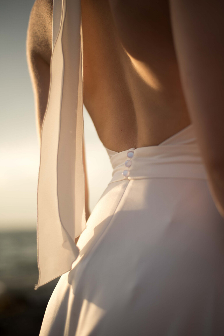 Close-up detail of the Unona Mary dress open back with fabric-covered buttons and silk ties