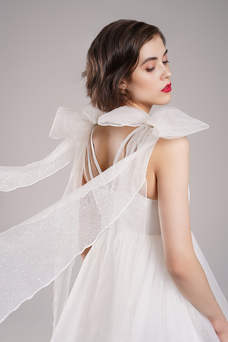 Close up of Leoni short ivory party dress back details. Features a delicate crisscross open back and glitter tulle fabric.