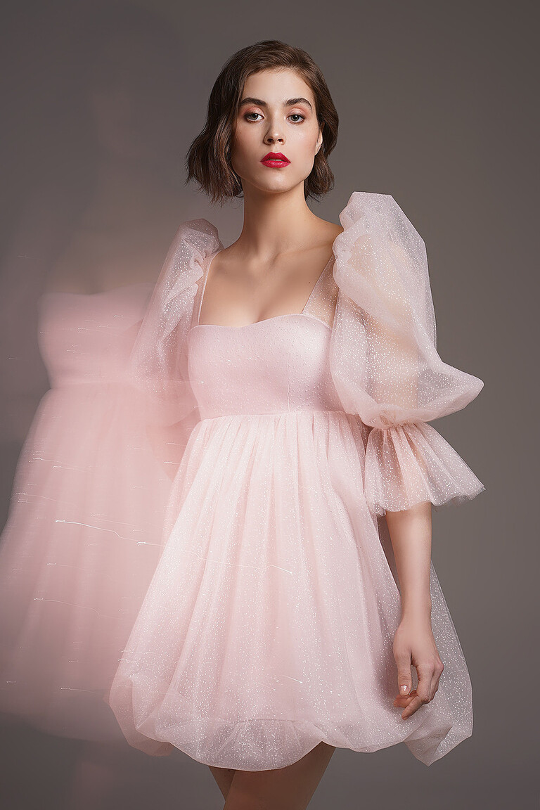 Lessi powder occasion dress modeling shot. Delicate short baby doll style with a fitted bodice and shimmering mesh overlay.