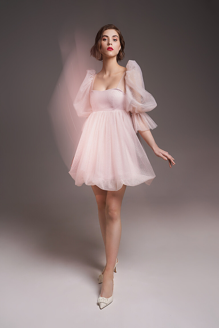 Lessi short powder occasion dress front view. Features a high waistline, glitter tulle, and voluminous puff sleeves.