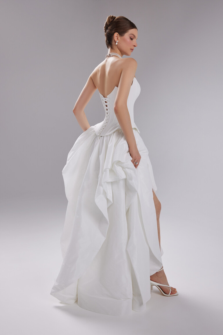 Back-angle view of the Sonara off-white couture gown displaying the lace-up back and dramatic thigh-high skirt slit.