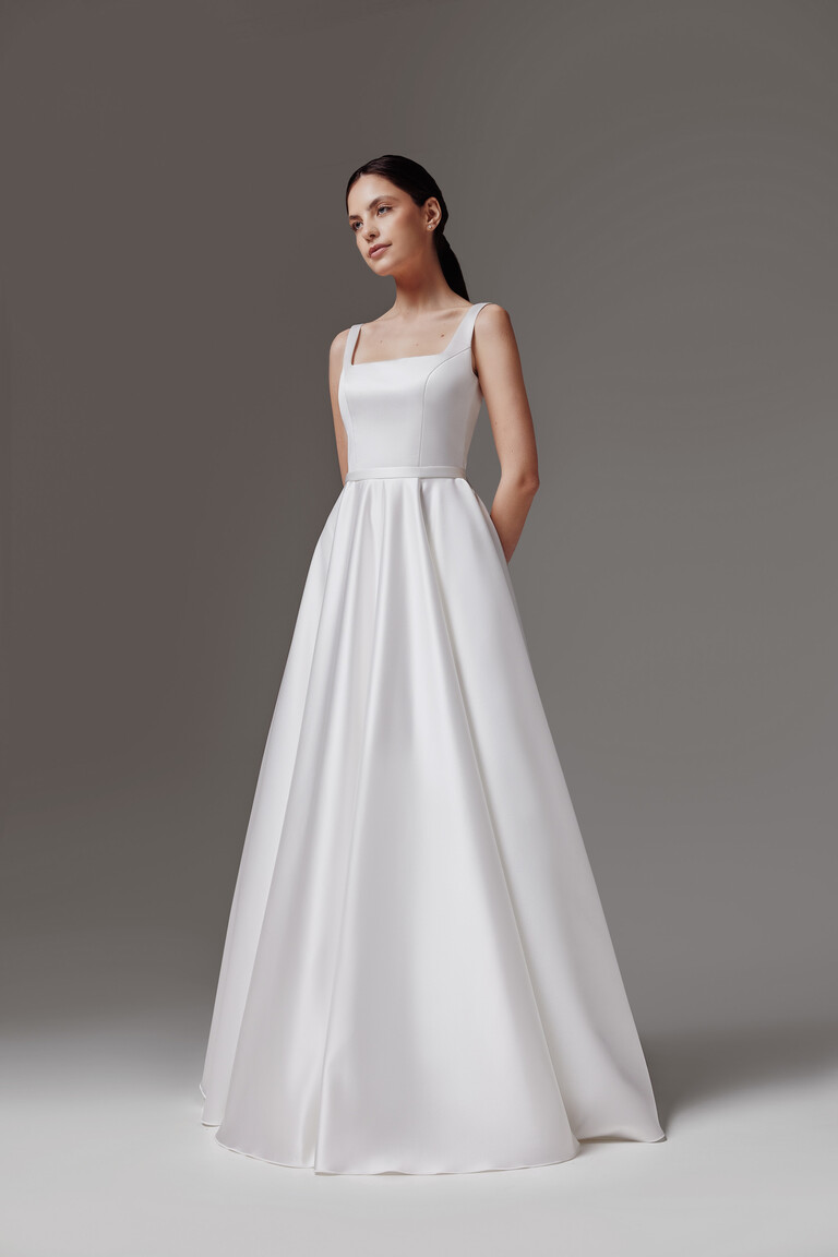 Full length angled view of the Vlada modern off-white satin wedding dress with a clean square neckline by Unona