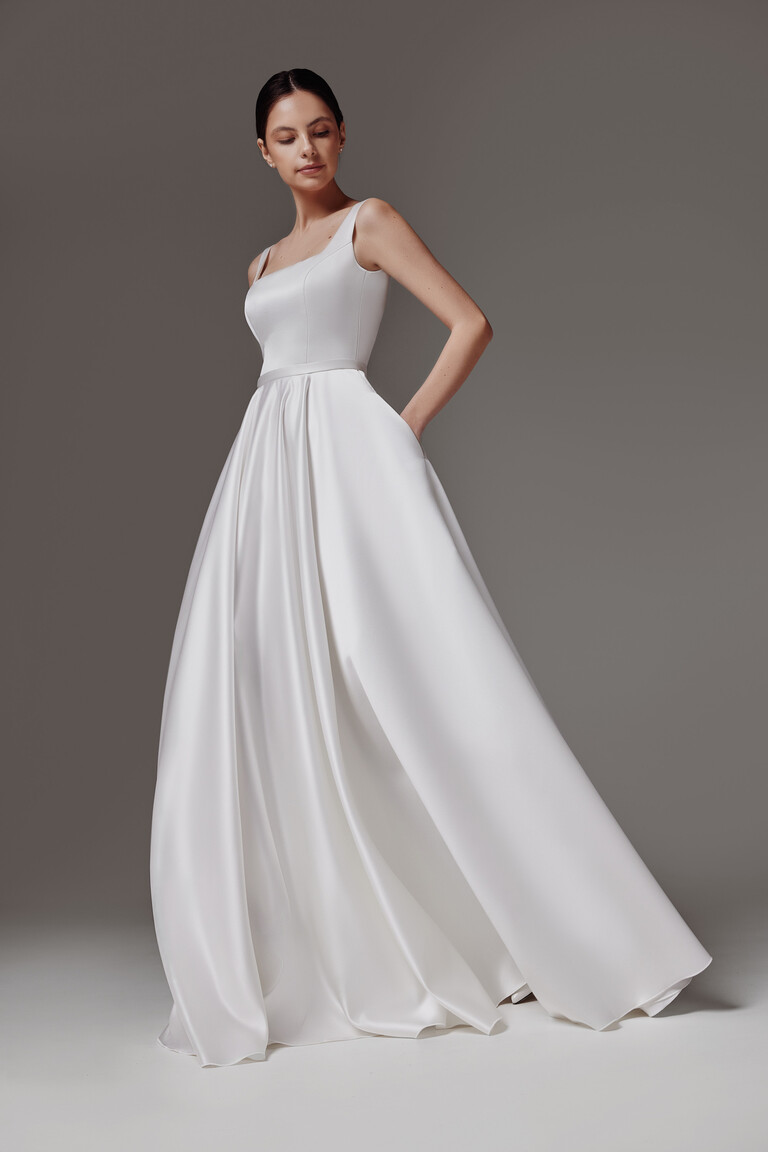 Front three-quarter view of the Vlada off-white minimalist wedding dress featuring a square neck and side pockets