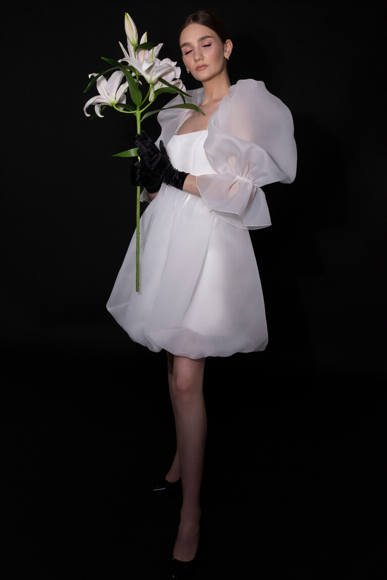 Styled front view of Lessi short ivory bridal dress by Unona. Features shimmering tulle puff sleeves and a balloon skirt.