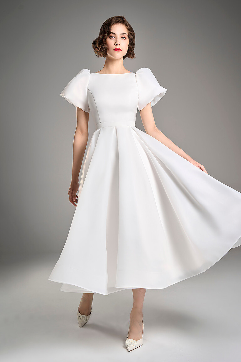 Bride holding the flowing organza skirt of the Audrey midi ivory A-line wedding dress by Unona