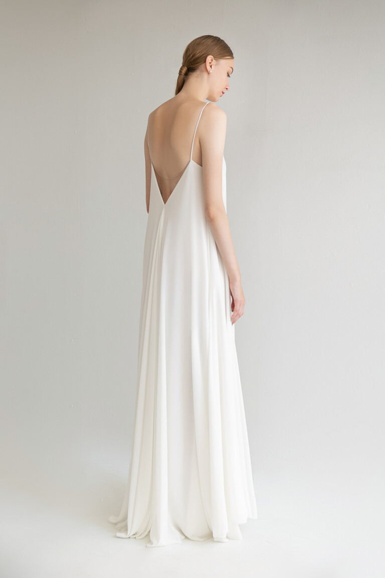 Three-quarter back view of the Unona Isa sleeveless wedding dress in ivory, highlighting its deep V-shaped open back and flowing silhouette.