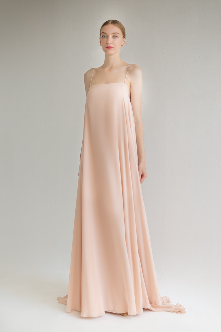Front view of the Isa peach slip dress showing its A-line trapeze silhouette and delicate puddle train on the floor.