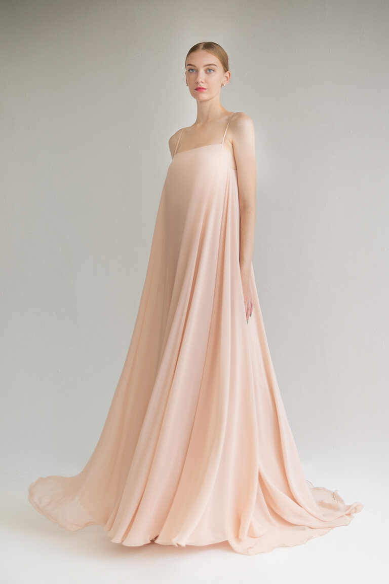 The Isa peach chiffon dress front view with its voluminous trapeze silhouette and floor-length skirt pooling at the feet.