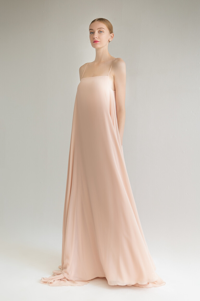 Model wearing the Unona Isa peach chiffon evening dress front view showcasing its loose floor-length silhouette.