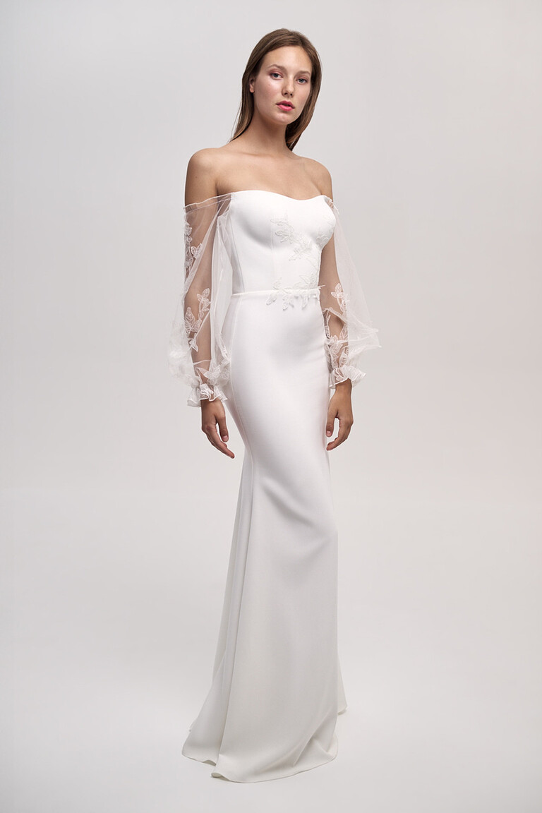 Discover the Fleur Off-the-Shoulder Crepe Wedding Dress Front view of Fleur off-white crepe wedding dress with sheer off-the-shoulder lace sleeves and fitted silhouette.
