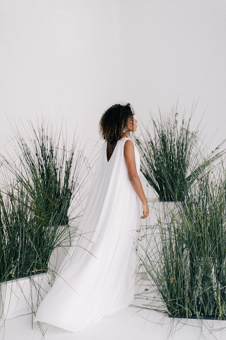 Three-quarter back of the Joan wedding dress showcasing its flowing cape panels that create a deep V-back on the ivory gown.
