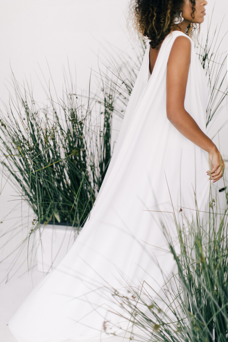 Back three-quarter view of the Joan bridal gown with its long chiffon train. A sleeveless ivory dress with a deep open back.