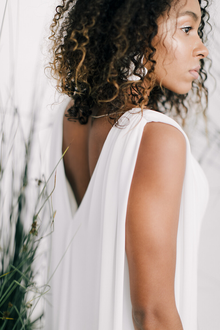 Closeup side-back detail of the Joan dress. Showing the draped chiffon shoulder and deep V-back on this sleeveless ivory gown.