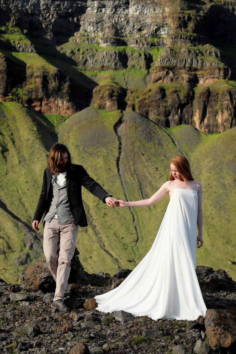 Unona Isa ivory wedding dress outdoors. The minimalist A-line gown with a long flowing train against a mountain backdrop.