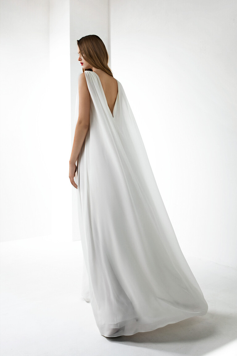 Full back view of the Unona Joan gown showing the deep V-back and floor-length cape-like train of the ivory chiffon dress.