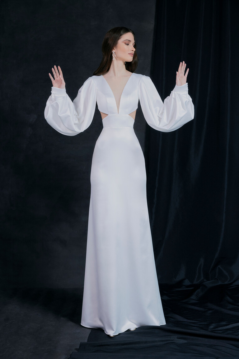 Modern Hannah Bridal Gown with Dramatic Long Sleeves Front view of Hannah modern ivory mermaid bridal gown featuring side cutouts and voluminous sleeves on a dark background.